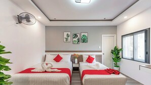 A hotel room with two beds, a ceiling fan, wall art, a potted plant, and a window.