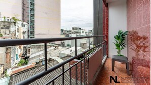 A hotel balcony with a view of the cityscape, a potted plant, and a bench.