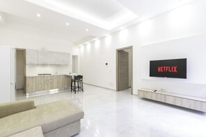 Un saló modern amb un televisor de pantalla plana, un sofà i una zona de cuina al fons.