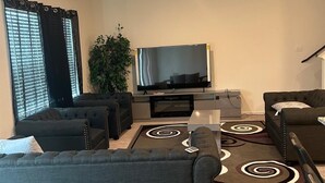 En moderne stue med en grå sofa, et fladskærms-tv og en dekorativ måtte.