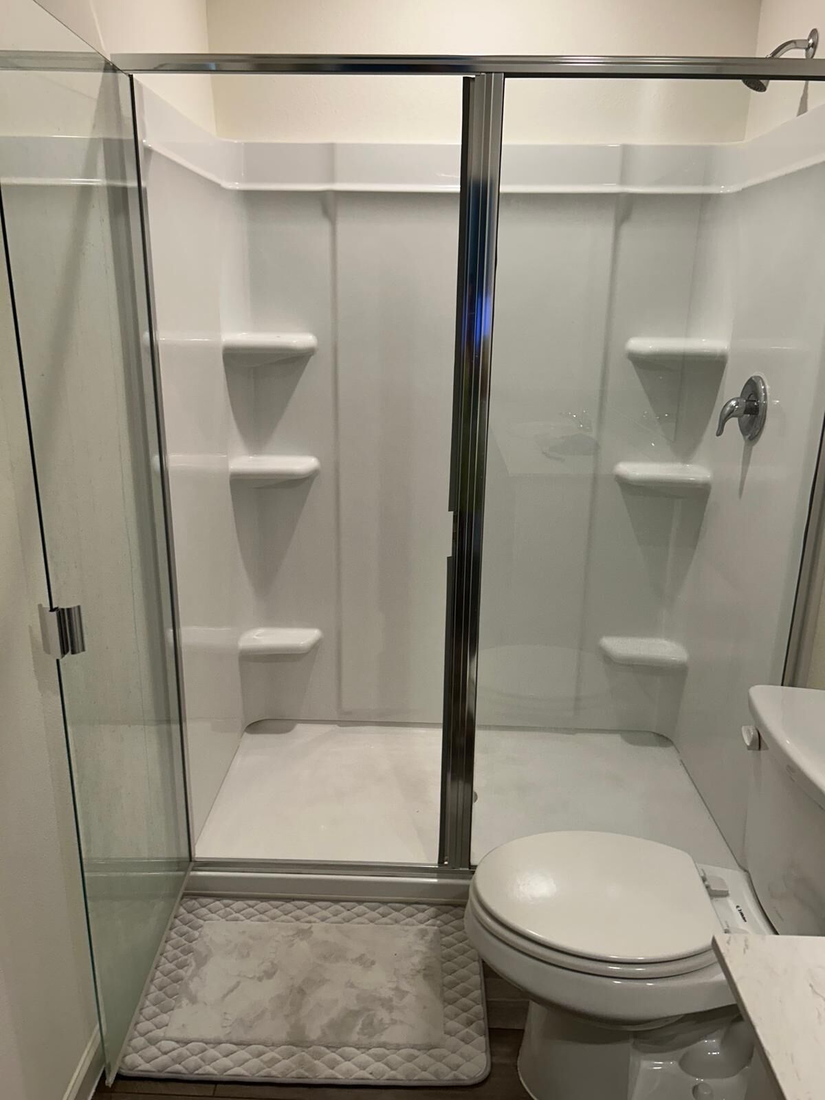 A modern bathroom with a glass-enclosed shower, a white toilet, and a marble countertop.