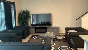 En moderne stue med et fladskærms-tv, mørke sofaer, et sofabord og en gulvtæppe med et mønster.