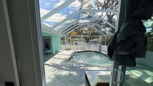 A glass door leading to a covered outdoor area with a pool, a lounge chair, and a view of a house with a green roof.