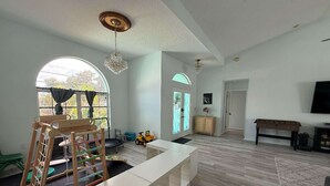 A spacious living room with a high ceiling, a large window, a wooden play area, and a white entertainment unit.