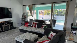 A living room with a large flat-screen TV, a fireplace, a Christmas tree, and a view of a pool and beach.