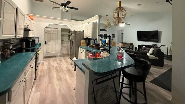 A modern kitchen with a central island, a dining area with bar stools, a ceiling fan, and recessed lighting.
