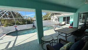 A covered outdoor area with a pool, seating, and a view of the backyard.