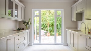 Une cuisine moderne avec des meubles blancs, une grande fenêtre et une vue sur un jardin.
