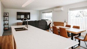 Eine moderne Küche mit einer zentralen Kochinsel, Essbereich mit Stühlen, einer Couch und einem an der Wand montierten Fernseher.