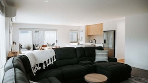 Ein modernes Wohnzimmer mit einem Ecksofa, einem runden Couchtisch und Blick auf die Küche im Hintergrund.