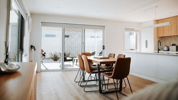 Eine moderne Küche mit Essbereich, ausgestattet mit einem Holztisch und -stühlen, einer Schiebeglastür zum Patio und Blick ins Freie.