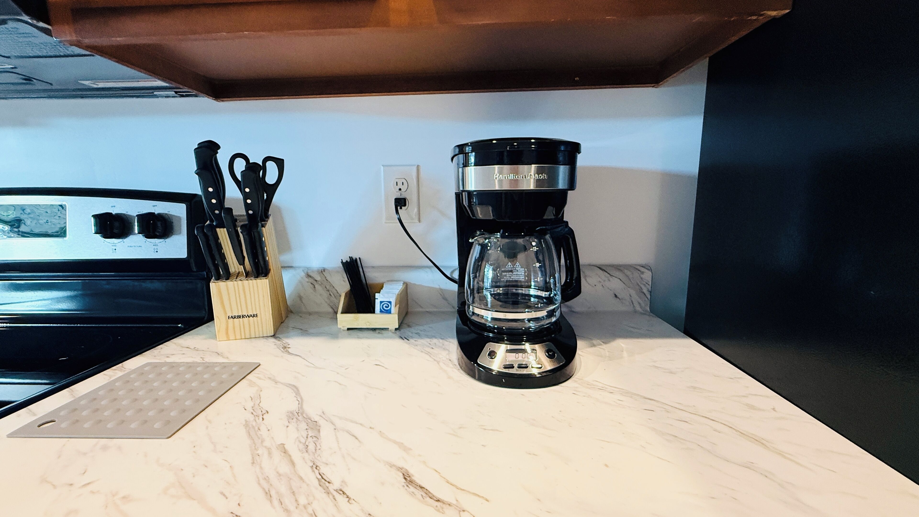 A kitchen counter with a coffee maker, a knife block, and a stove.