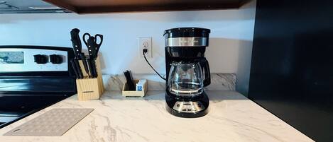 A kitchen counter with a coffee maker, a knife block, and a stove.