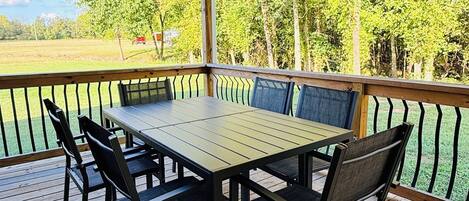 Een overdekt terras buiten met een houten tafel en stoelen, omgeven door een metalen hekwerk.