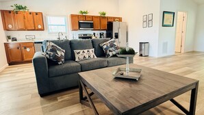 A modern living room with a grey sofa, wooden coffee table, and kitchen in the background.