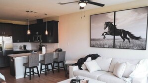Een moderne woonkamer met een bank, salontafel en een eethoek met stoelen, en een keuken op de achtergrond.