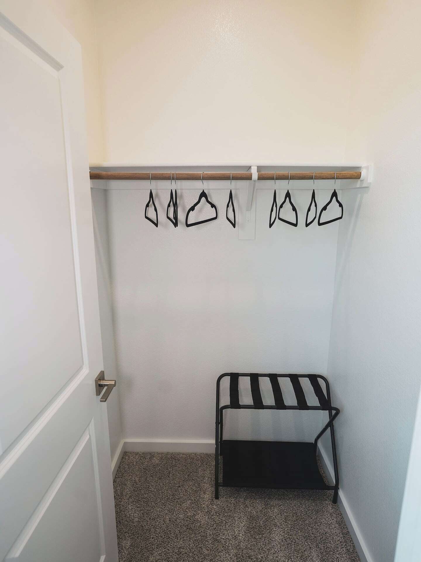 A small, clean room with a white door, a bench with black and white stripes, and a clothes rack with black hangers.
