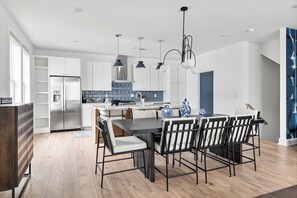 A modern kitchen with white cabinets, a stainless steel refrigerator, and a dining area with a dark table and striped chairs.