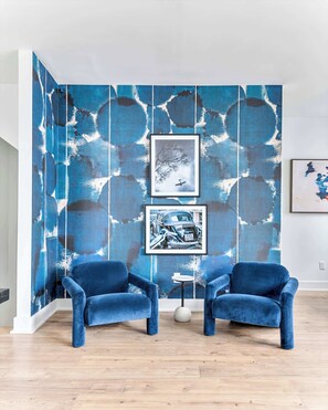 A room with two blue velvet armchairs, a small round table, and a wall with abstract blue and white patterns.