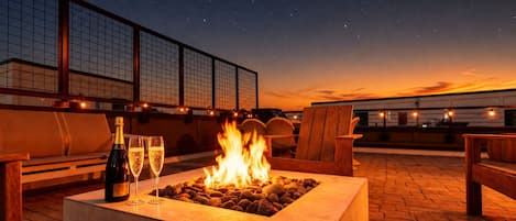 Une terrasse sur le toit avec un foyer, des sièges d’extérieur et une bouteille de champagne.