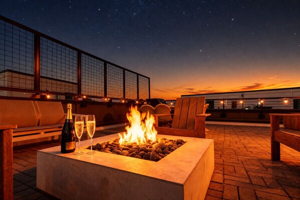 A rooftop terrace with a fire pit, outdoor seating, and a bottle of champagne.