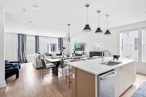 A modern kitchen with a central island, a dining area with a sofa and chairs, and a living room with a TV. - Rooftop fire pit house with skyline views, sleeps 10 near Broadway, Nashville (Nashville)