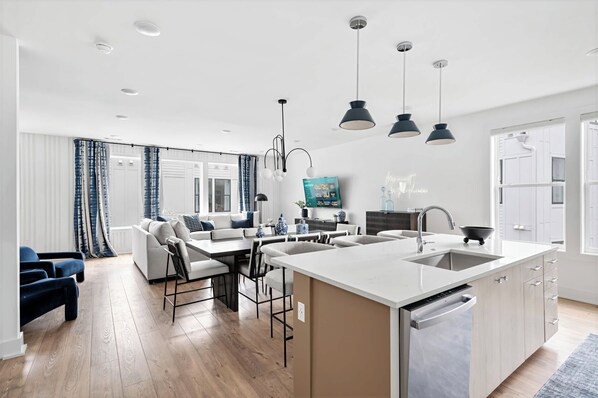 A modern kitchen with a central island, a dining area with a sofa and chairs, and a living room with a TV. - Rooftop fire pit house with skyline views, sleeps 10 near Broadway, Nashville (Nashville)
