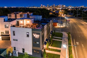 A modern building with a prominent sign 'THE LUCY' on the facade, a parking lot, and a view of a city skyline in the background.