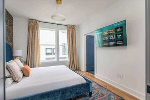 A modern hotel room with a bed, curtains, a television, and a view of the outside. - Fall in Nashville: dog-friendly 3BR house, sleeps 10, near Germantown (Nashville)