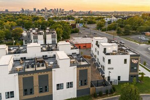 A multi-story building with a rooftop terrace, a parking lot, and a view of a city skyline. - Fall in Nashville: designer 3BR home, sleeps 10, pet friendly, Germantown (Nashville)