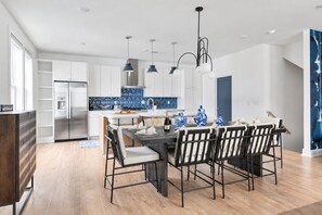 A modern kitchen with a dining area, featuring a stainless steel refrigerator, a blue tiled backsplash, and a dining table set for six.