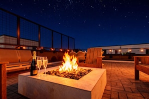 A rooftop terrace with a fire pit, seating, and a bottle of champagne.
