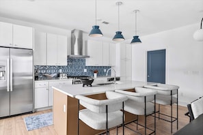 A modern kitchen with white cabinets, a stainless steel refrigerator, a blue backsplash, and a central island with bar stools. - Rooftop fire pit house with skyline views, sleeps 10 near Broadway, Nashville (Nashville)