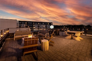 A rooftop terrace with outdoor seating, a fire feature, and a view of buildings under a sunset sky. - Fall in Nashville: dog-friendly 3BR house, sleeps 10, near Germantown (Nashville)