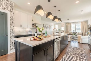 A modern kitchen with a central island, stainless steel appliances, pendant lighting, and a dining area with a sofa and coffee table. - Fall getaway: 4BR Nashville home with gold-tile shower, sleeps 12 (Nashville)