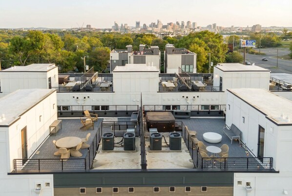 A rooftop terrace with seating, air conditioning units, and a city skyline view.