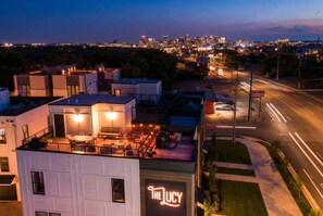 A modern building with a rooftop patio area, a sign reading "The Lucy," and a city skyline in the background.