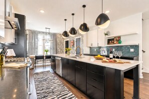 A modern kitchen with a central island, black cabinets, and pendant lighting.