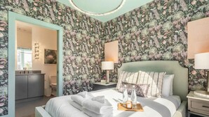 A bedroom with floral wallpaper, a bed with towels, a bedside table with a lamp, and a nightstand with a lamp. - Nashville 4-bedroom house with gas grill, sleeps 12, pet friendly (Nashville)