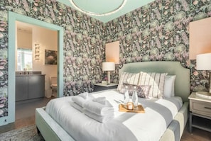A bedroom with floral wallpaper, a bed with towels, a bedside table with a lamp, and a nightstand with a lamp.
