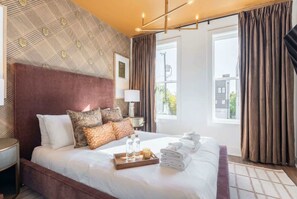 A hotel room with a large bed, a bedside table, a lamp, and a window with curtains.
