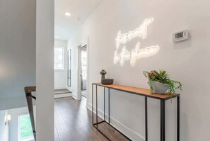 A modern hallway with a neon sign, a console table with a plant, and a digital thermostat on the wall. - Fall getaway: 4BR Nashville home with gold-tile shower, sleeps 12 (Nashville)