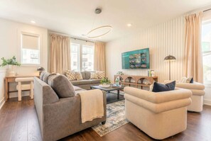 A modern living room with a sofa, armchairs, a coffee table, and a TV mounted on the wall.