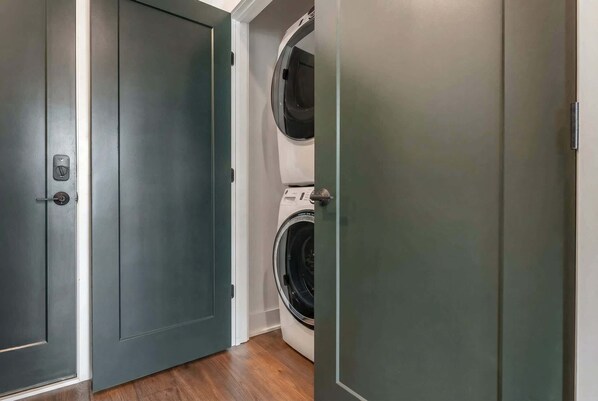 A laundry room with two washing machines, a door, and wooden flooring.