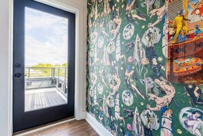 A room with a black door leading to a balcony, a green wall with comic book-style wallpaper, and a colorful patterned area on the right.