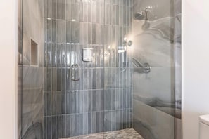 A modern bathroom with a glass-enclosed shower, a marble-tiled wall, and a small window.
