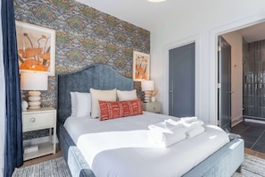 A modern bedroom with a large bed, two bedside tables, a headboard, and a patterned wall.