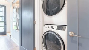 A laundry room with two stacked front-loading washing machines, a door with a mirror, and a window with a view of the outside. - Fall in Nashville: hot tub, skyline views, sleeps 12 near Broadway (Nashville)