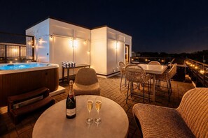 Una terraza en la azotea con un jacuzzi, muebles de mimbre, una mesa con copas y una botella de champán.