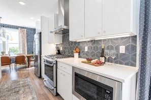 A modern kitchen with stainless steel appliances, a dining area with a wooden table and chairs, and a patterned backsplash. - Fall hot tub deck house, sleeps 12 near Germantown, Nashville (Nashville)